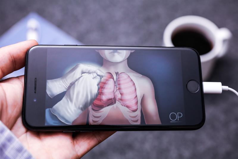 A smartphone shows an illustration of gloved hands operating on organs under rib bones.